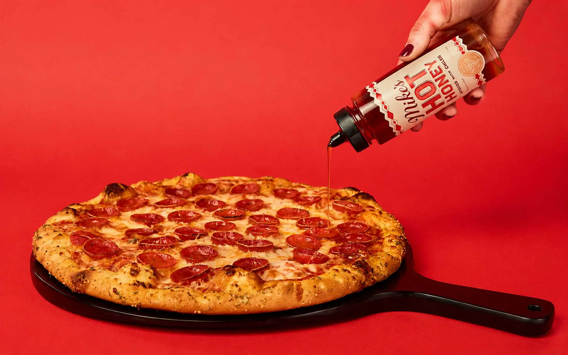 Pepperoni pizza with Mike’s Hot Honey® being drizzled on it.