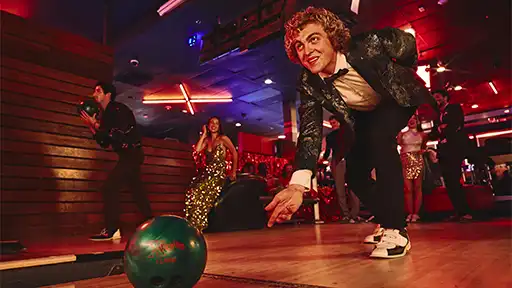 Group enjoying a holiday bowling party at Lucky Strike, with a bowler in a tuxedo rolling a ball on the lanes during a festive celebration.