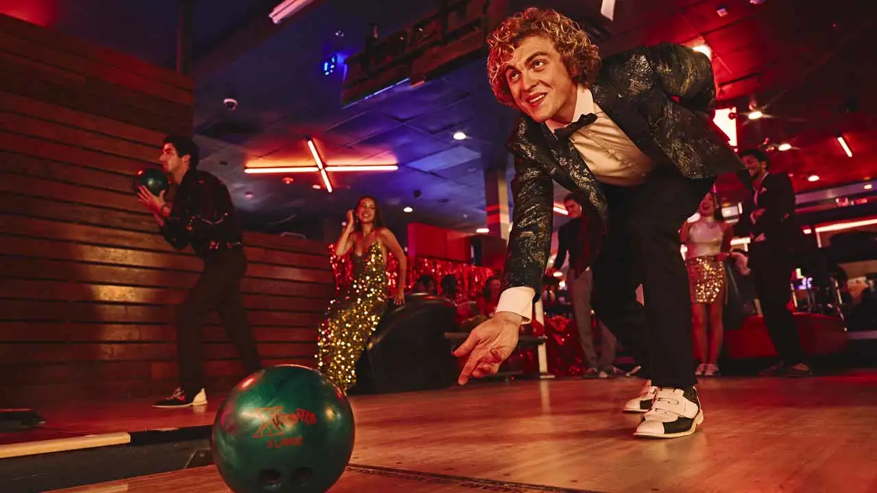 Group enjoying a holiday bowling party at Lucky Strike, with a bowler in a tuxedo rolling a ball on the lanes during a festive celebration.