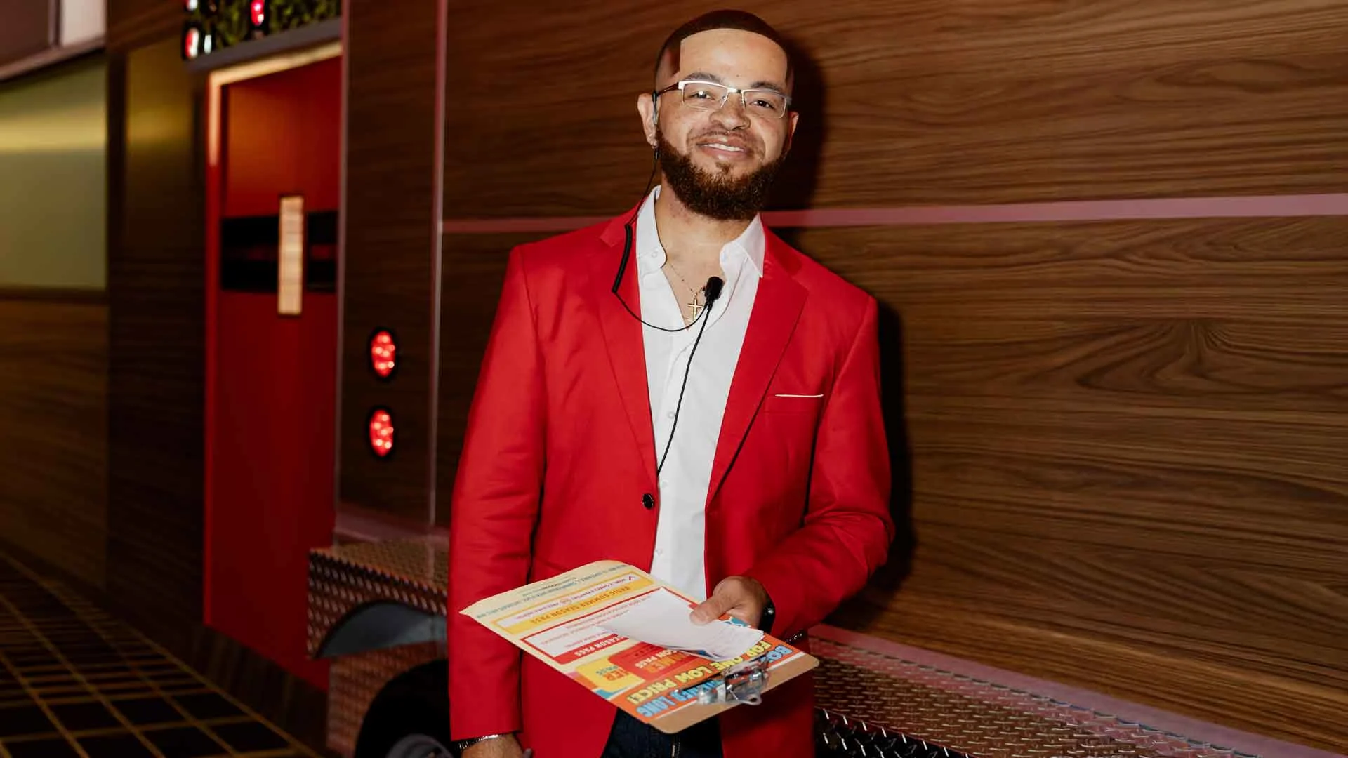 Lucky Strike Entertainment associate in a red blazer holding event materials inside a bowling center, smiling and welcoming guests.