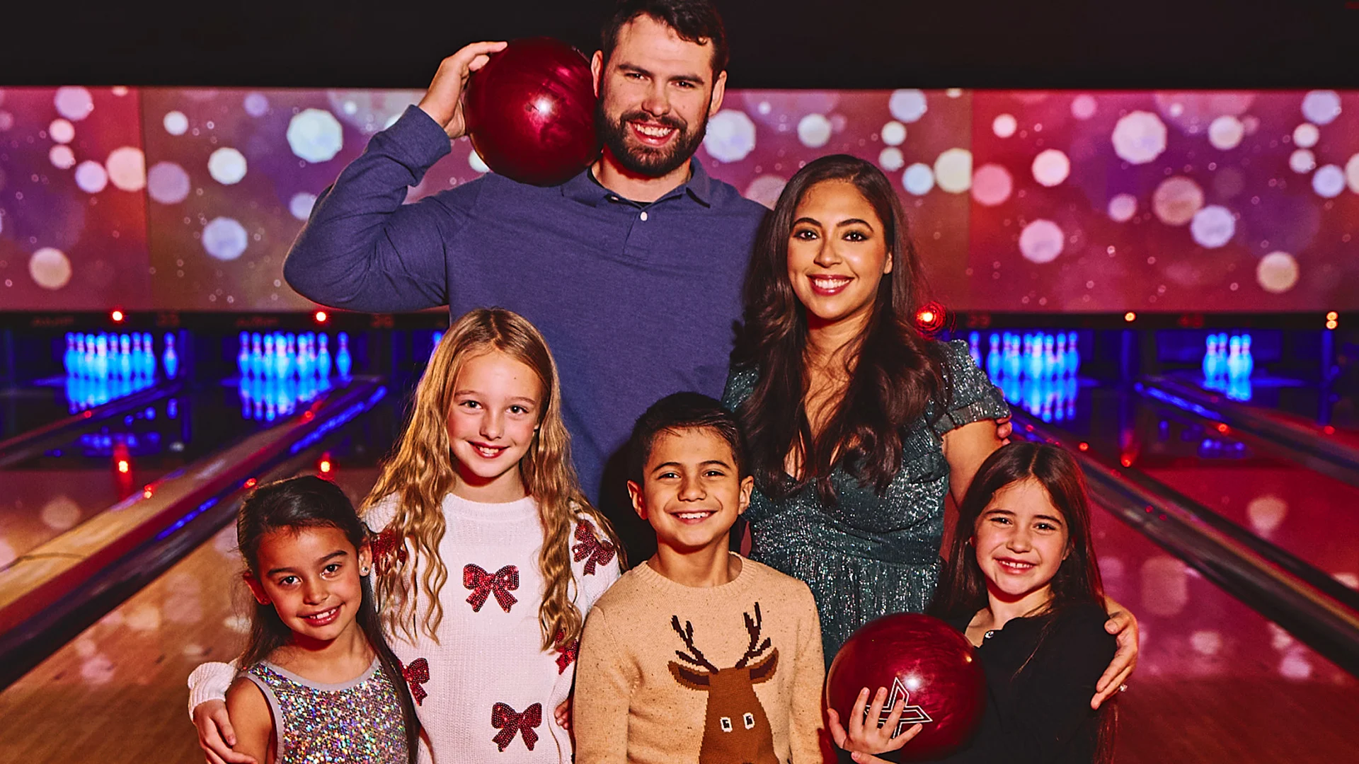 A family of 5 dressing in holiday attire standing in front of bowling lanes.