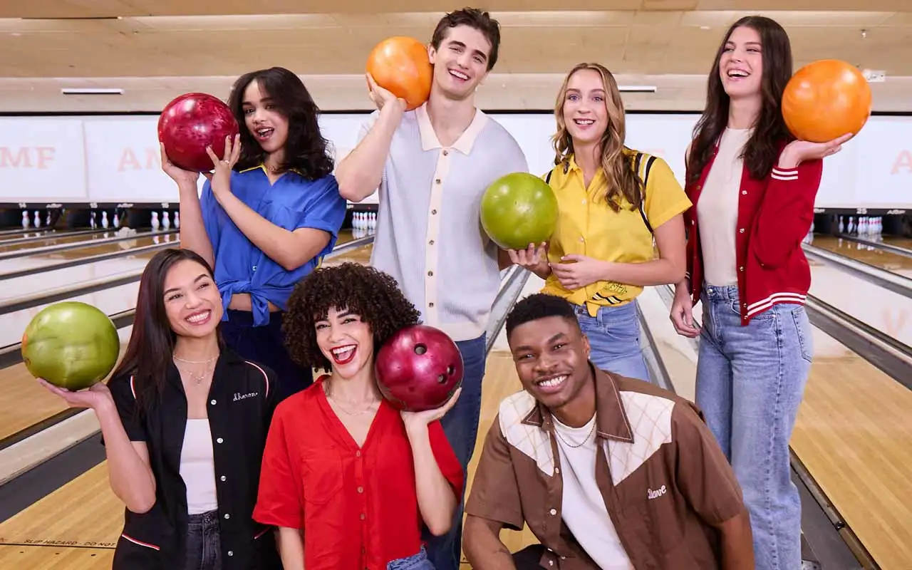 Group of friends smiling and holding colorful bowling balls on the lanes at an AMF bowling center.