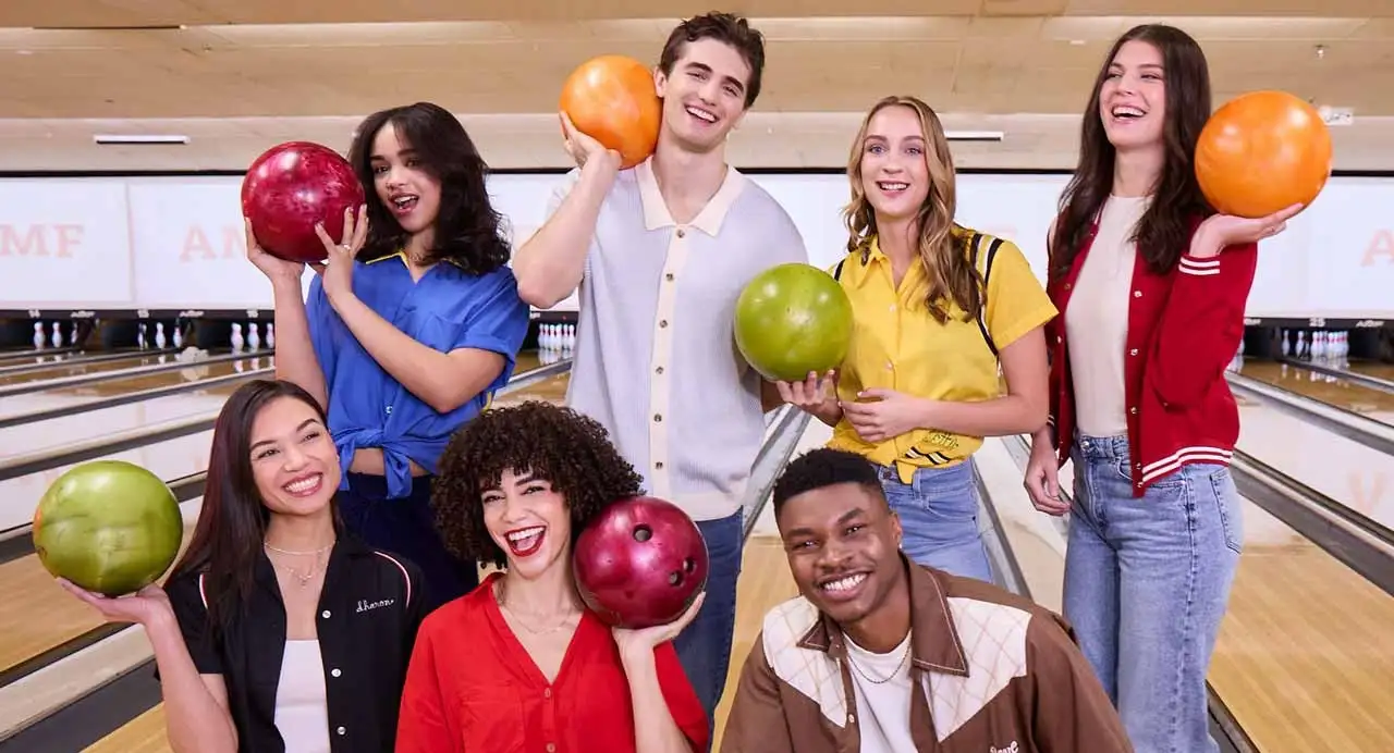 Group of friends smiling and holding colorful bowling balls on the lanes at an AMF bowling center.