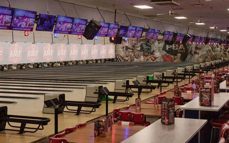 Wide view of an AMF bowling center showing rows of empty lanes, overhead score screens, and red diner seating along the concourse.