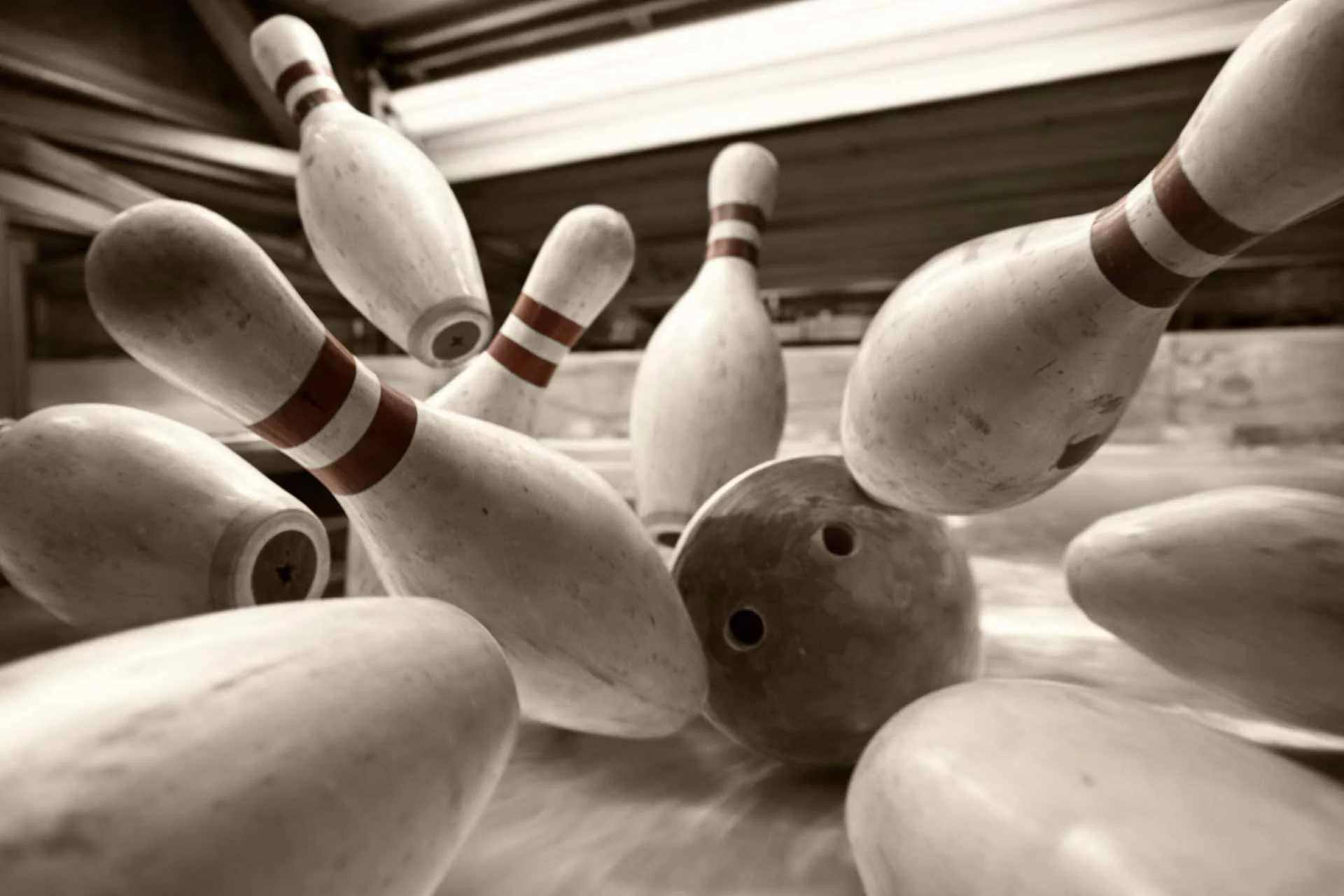 Bowling pins flying into the air as a bowling ball strikes them on the lane.