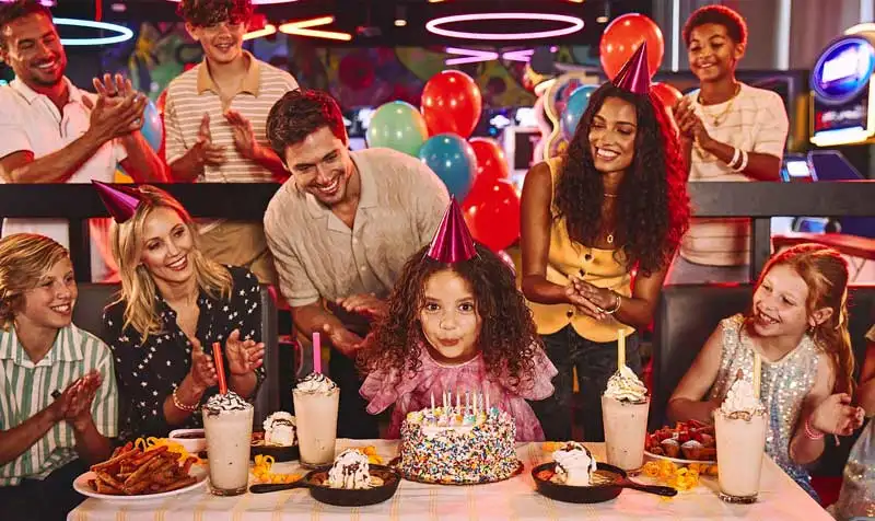 Child blowing out birthday candles at a Lucky Strike kids birthday party with family, arcade games, milkshakes, and desserts