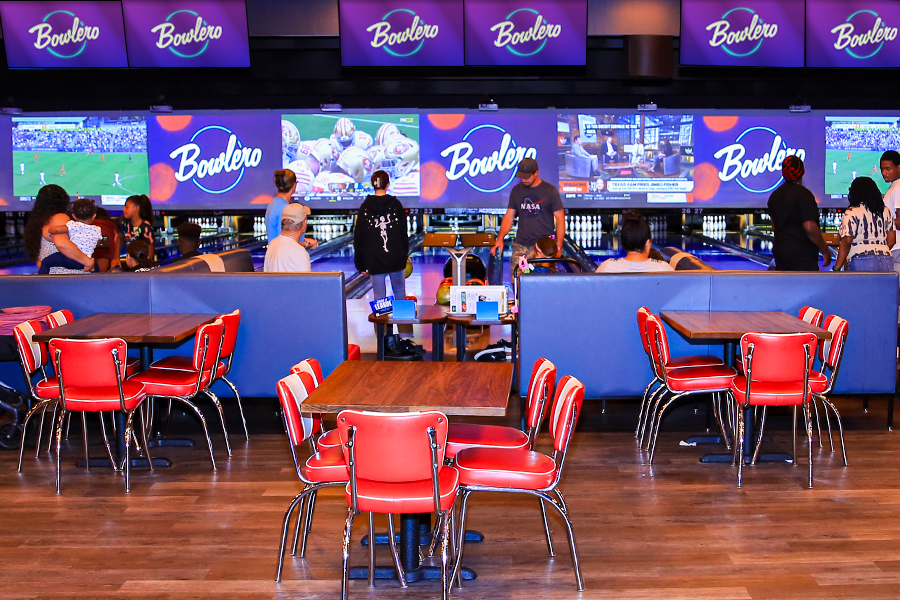 Tables and seats with bowling lanes and large TVs in the background