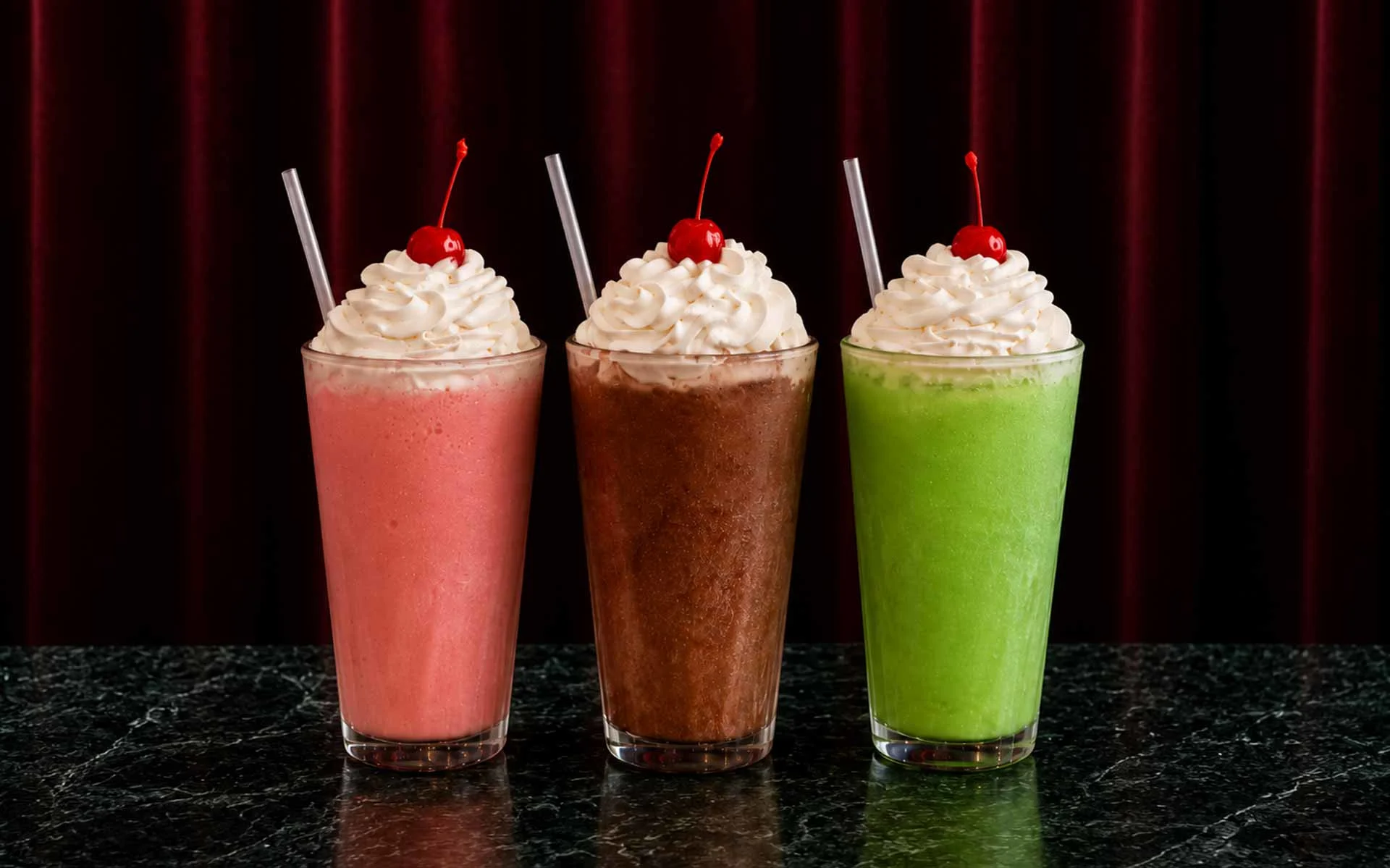 Cherry Lime, Vanilla Dr Pepper, and Sour Apple dirty sodas with whipped cream toppings on cherry-topped straws against red velvet curtain backdrop.