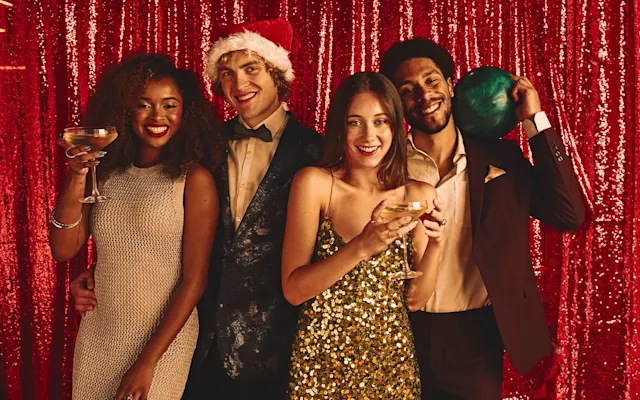 Four friends dressed up in holiday attire in front of a red sequence backdrop 