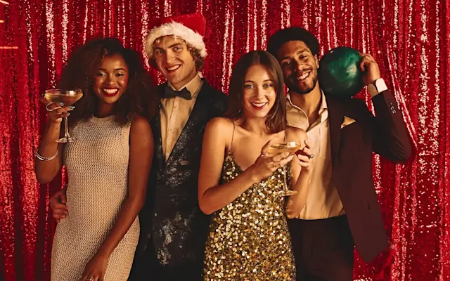 Four friends dressed up in holiday attire in front of a red sequence backdrop 