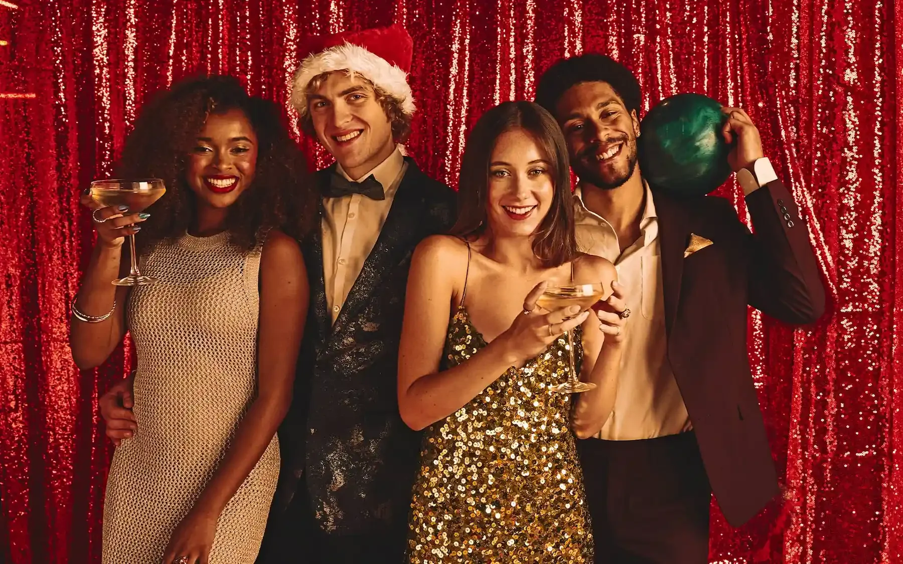 Four friends dressed up in holiday attire in front of a red sequence backdrop