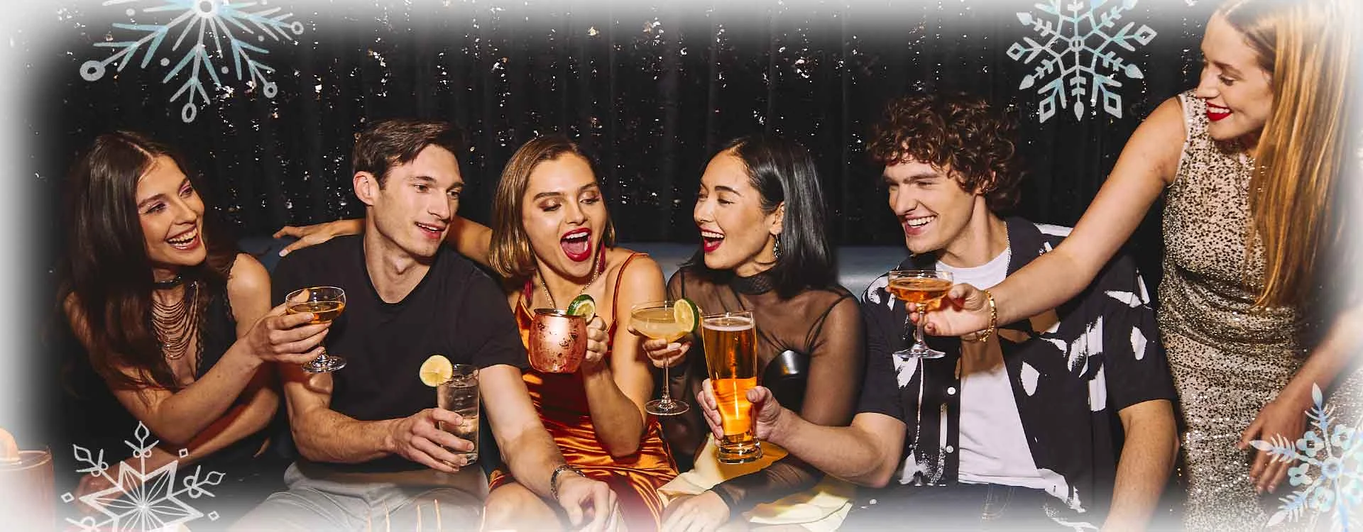 A group of six people at a table celebrating with drinks, with a winter-themed background