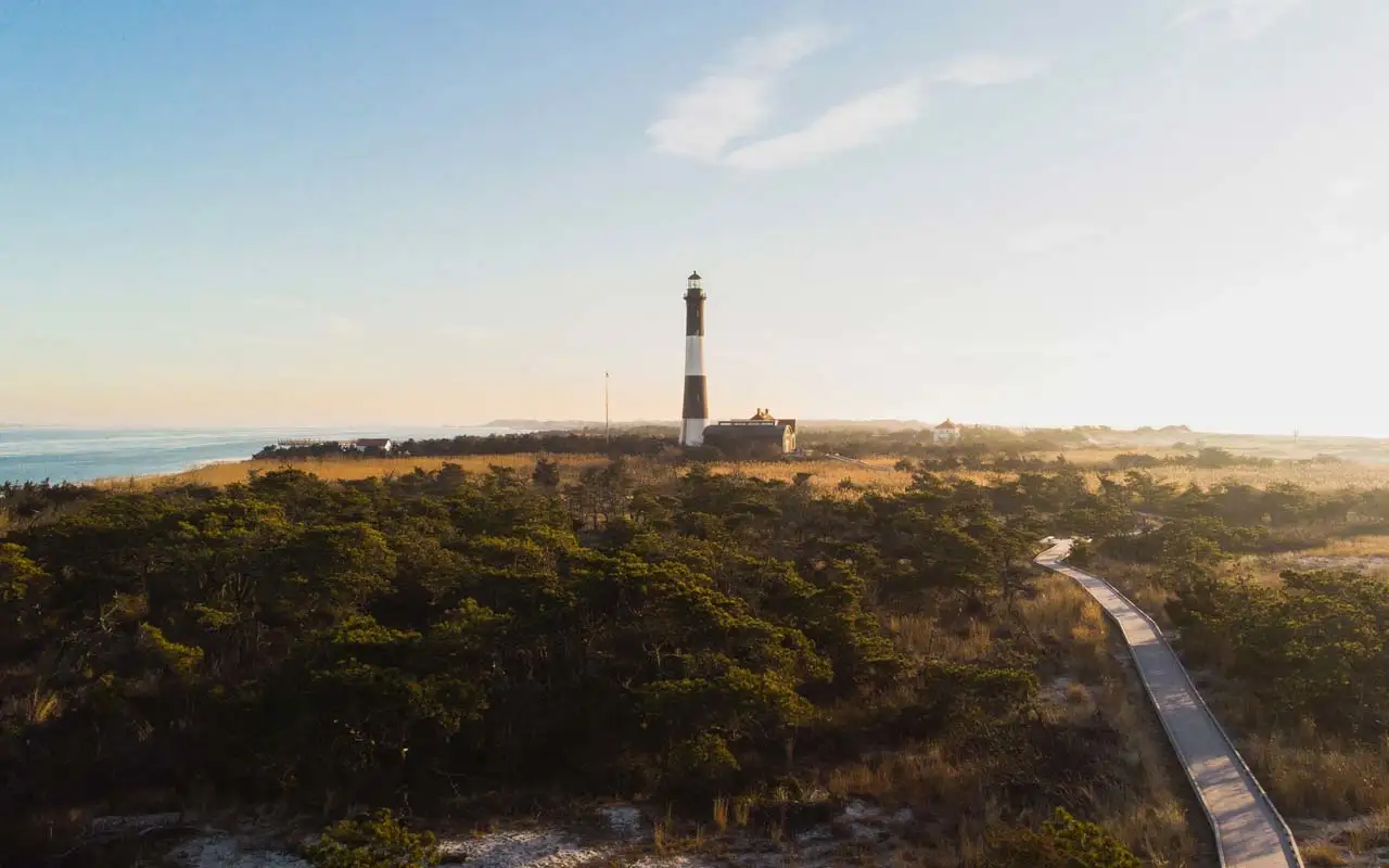 A lighthouse on Long Island, New York surrounded by ocean and greenery, with a walkway in the foreground.