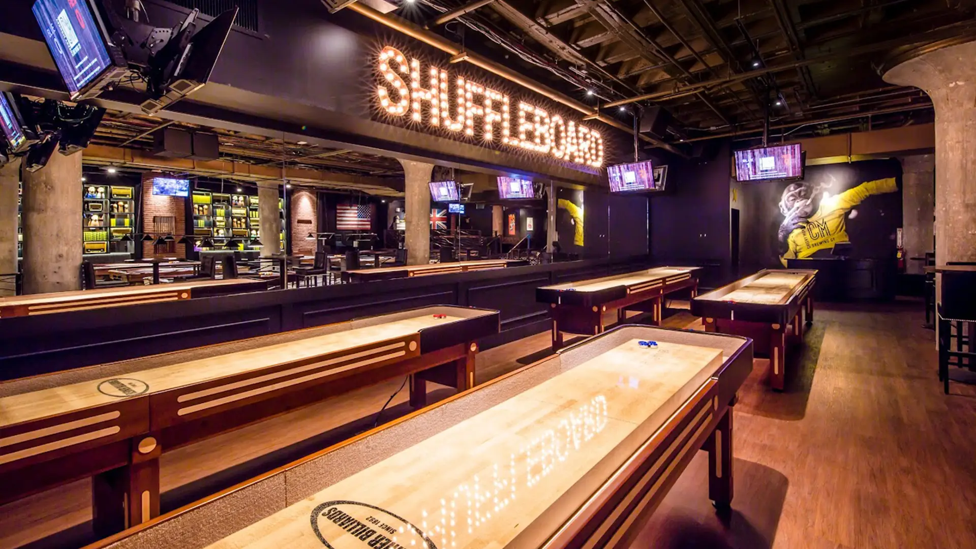 Cheeky Monkey shuffleboard area with multiple game tables, TVs, and neon signage.