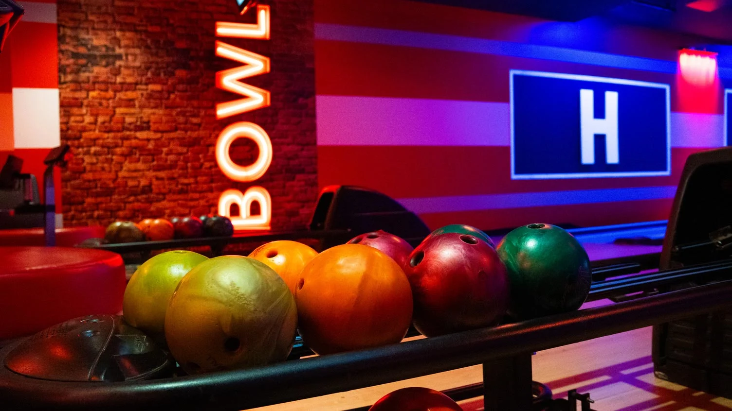 Colorful bowling balls at Lucky Strike with neon signage and a stylish bowling lane backdrop.