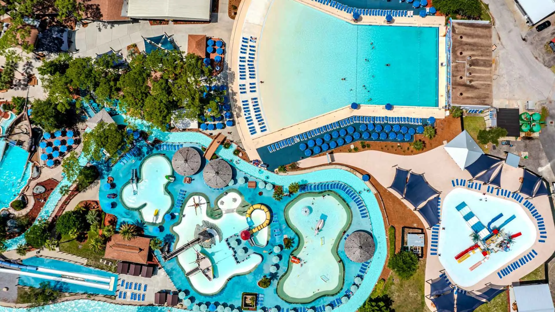 Aerial view of a large outdoor waterpark featuring pools, lazy rivers, waterslides, and shaded lounge areas.