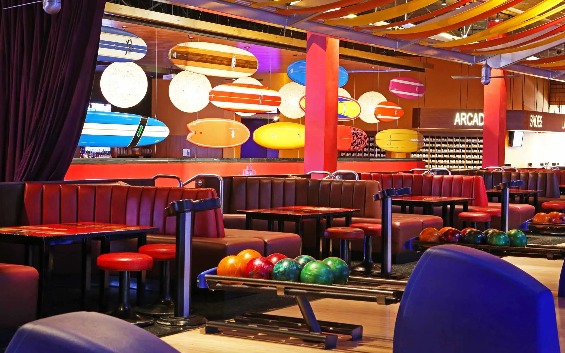 Stylish dining and lounge area with booth seating, wood tables, and modern lighting inside a Bowlero bowling and entertainment venue.