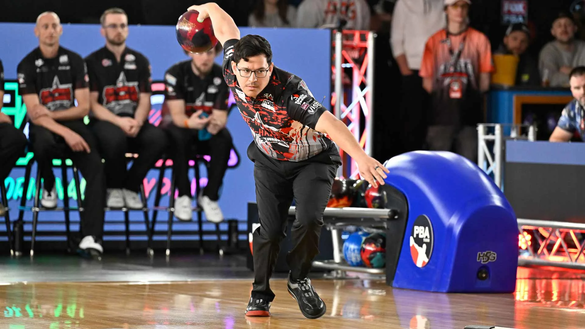 Professional bowler releasing a bowling ball during a PBA competition, with other players seated behind the lanes.