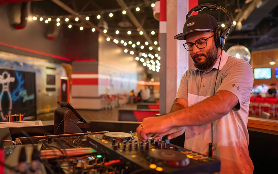 DJ at turn tables with bowling in the background