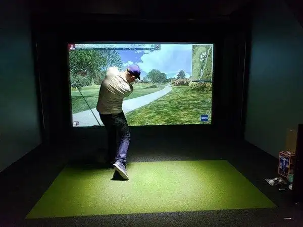 Person hitting gold ball toward a large golf simulated screen