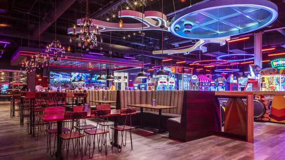 Bar and lounge seating area at Lucky Strike Dania Beach with arcade games, food truck counter, and neon signage