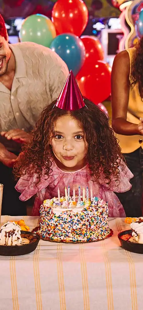 A birthday girl blowing out candles on a birthday cake at a Lucky Strike center.