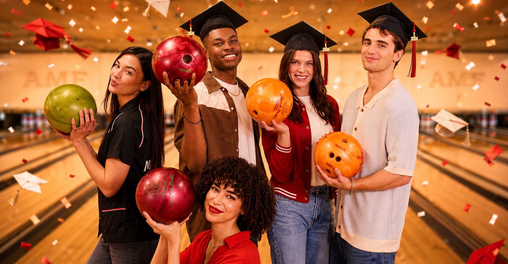 Group of recent college graduates posing with colorful bowling balls inside an AMF bowling alley, surrounded by red and white confetti and graduation caps in a warm, celebratory atmosphere.