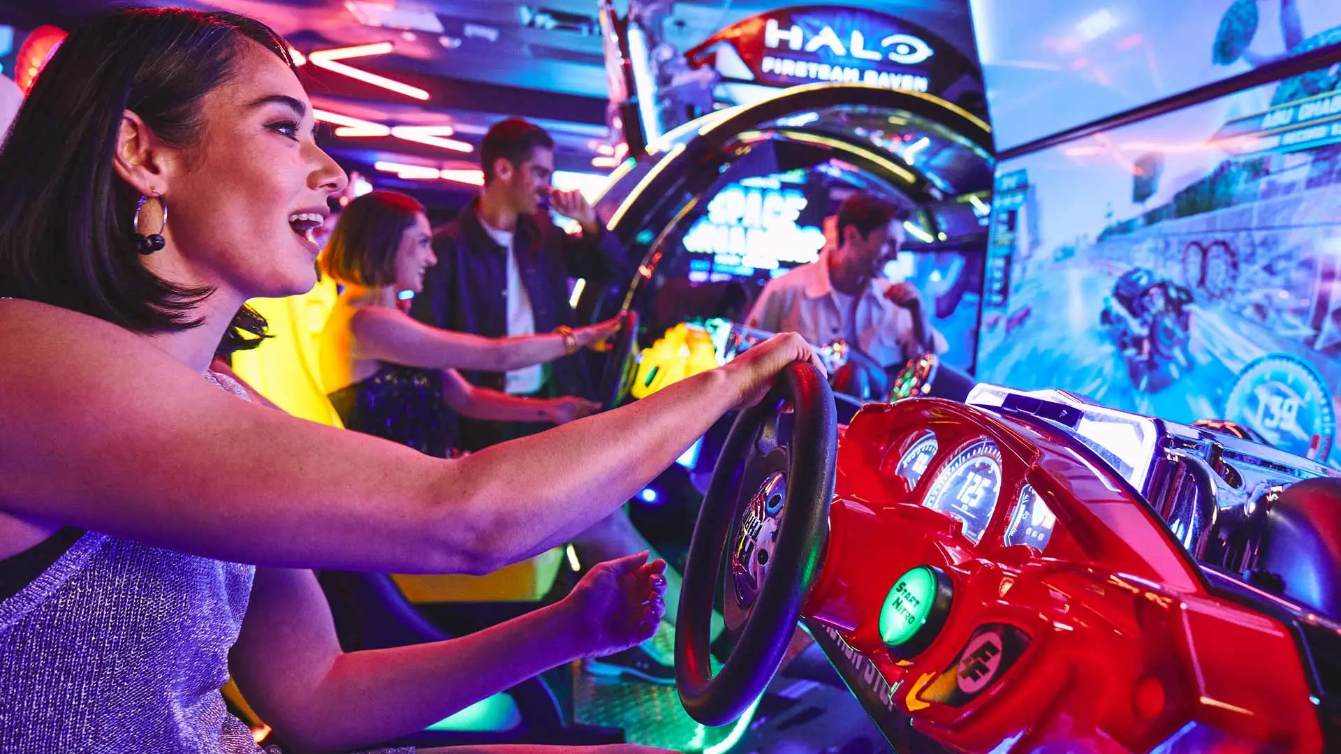Guests playing racing arcade games in a colorful arcade with glowing screens and interactive machines.