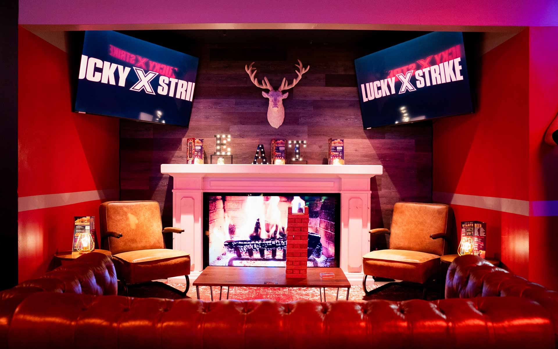Cozy lounge inside Lucky Strike featuring a fireplace, leather seating, mounted TVs, and warm ambient lighting for a premium social experience.