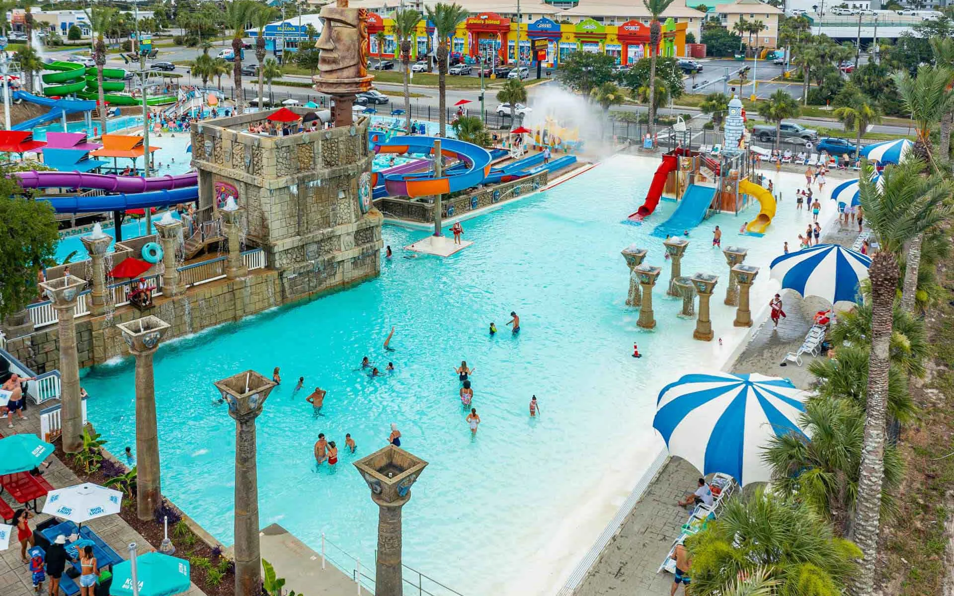Aerial view of Big Kahuna’s Water & Adventure Park showing a large wave pool, colorful water slides, palm trees, shaded lounge areas, and guests enjoying the water on a sunny day.