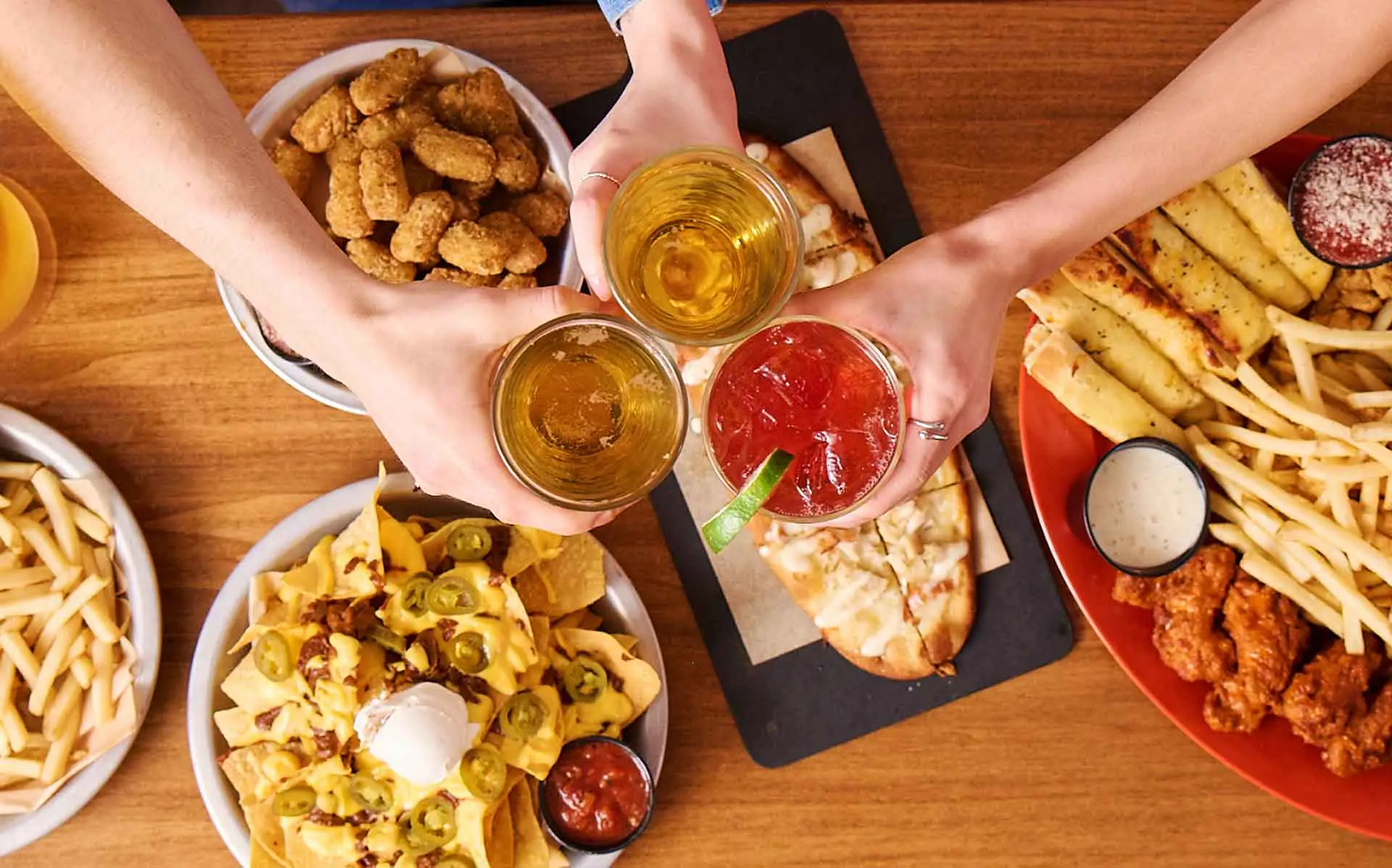 Friends toasting drinks over a table full of appetizers and shareable snacks at AMF.