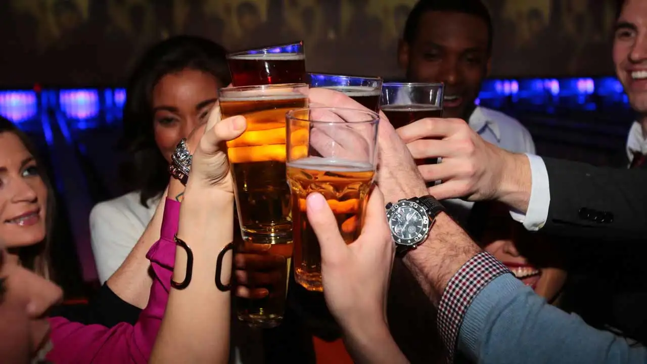 A group of friends cheersing with glasses of draft beer at a Lucky Strike bowling center.