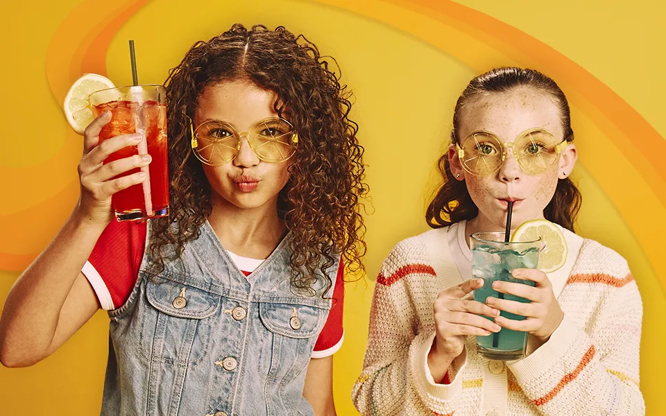 Two kids enjoying lemonade in front of a yellow background