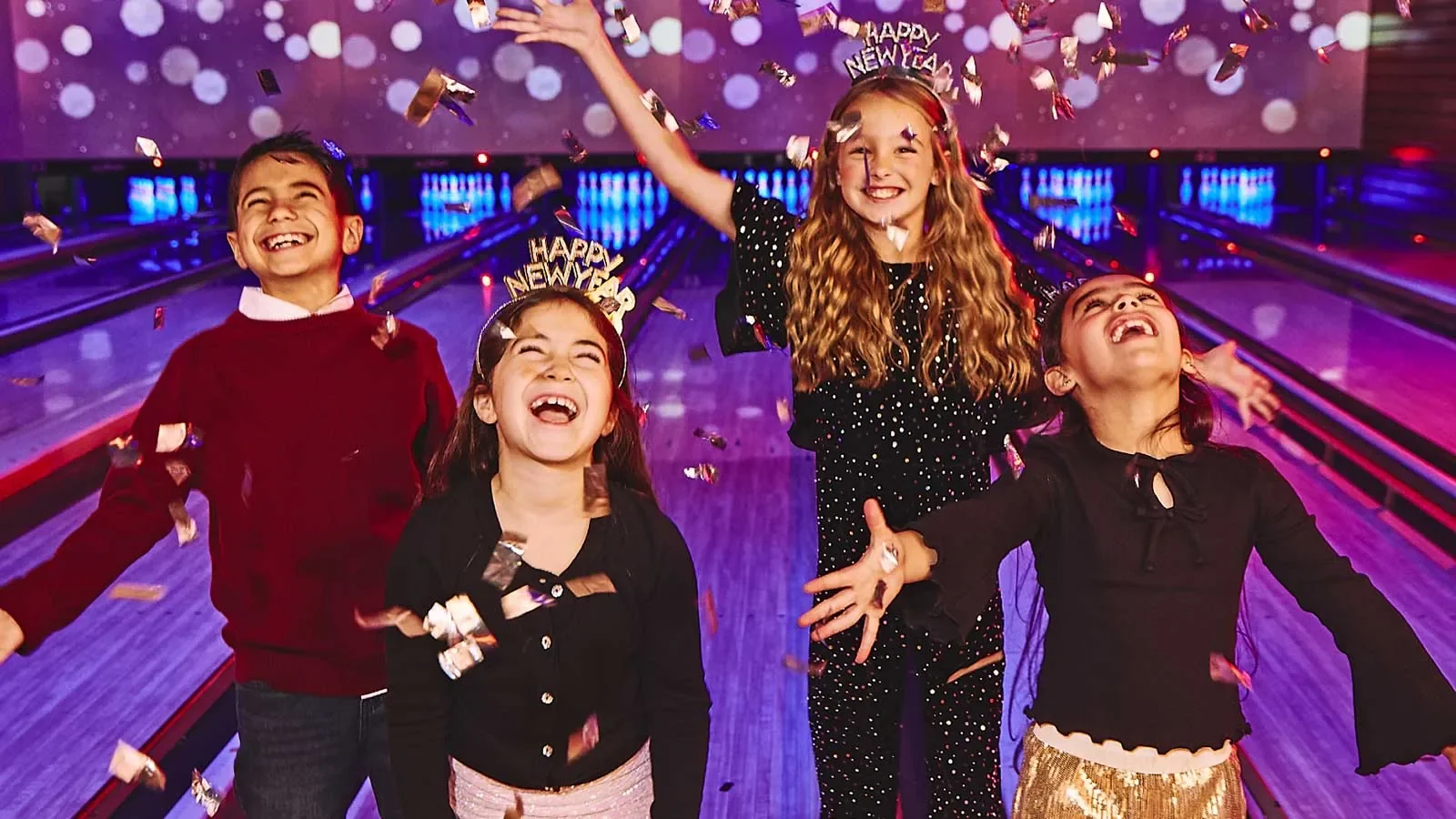 Four kids with New year tiaras celebrating in front of bowling lanes