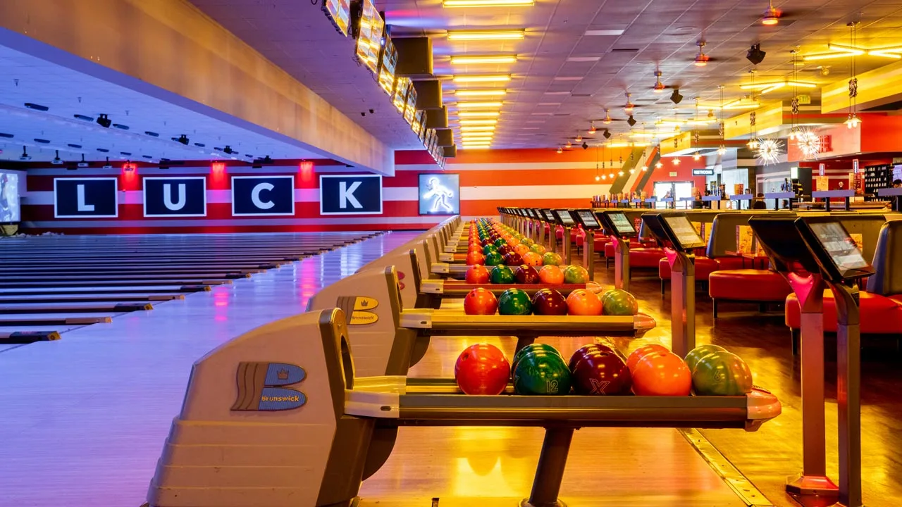 Colorful bowling balls lined up on return racks with bowling lanes in the background