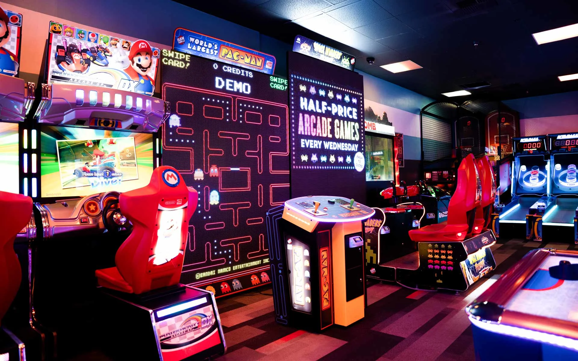 Modern arcade at Lucky Strike bowling venue featuring a giant Pac-Man screen, Mario Kart racing games, neon lighting, and colorful gaming machines.