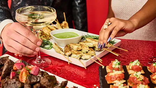 Holiday party appetizers including chicken skewers and cocktails on a festive red table at a Lucky Strike event.