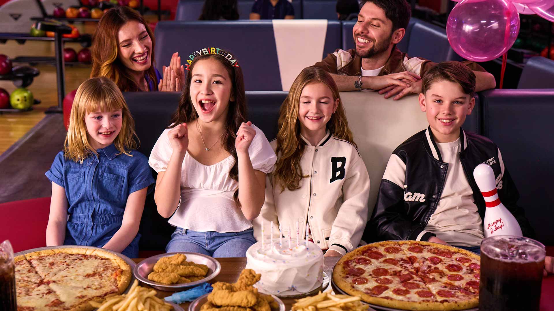 Kids celebrating a bowling birthday party at AMF with pizza, cake, fries, and family cheering in a bowling lounge.