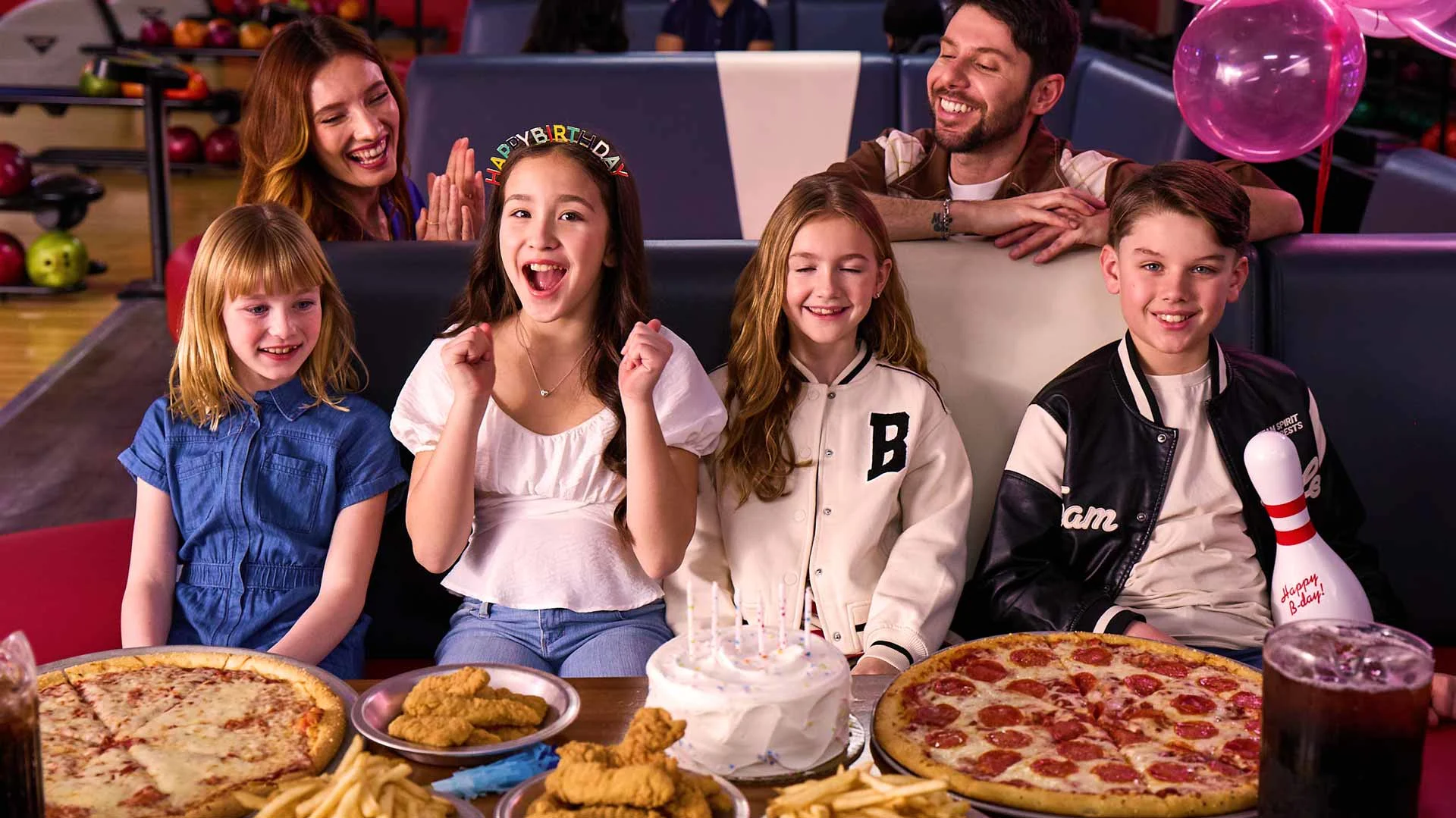 Kids celebrating a bowling birthday party at AMF with pizza, cake, fries, and family cheering in a bowling lounge.