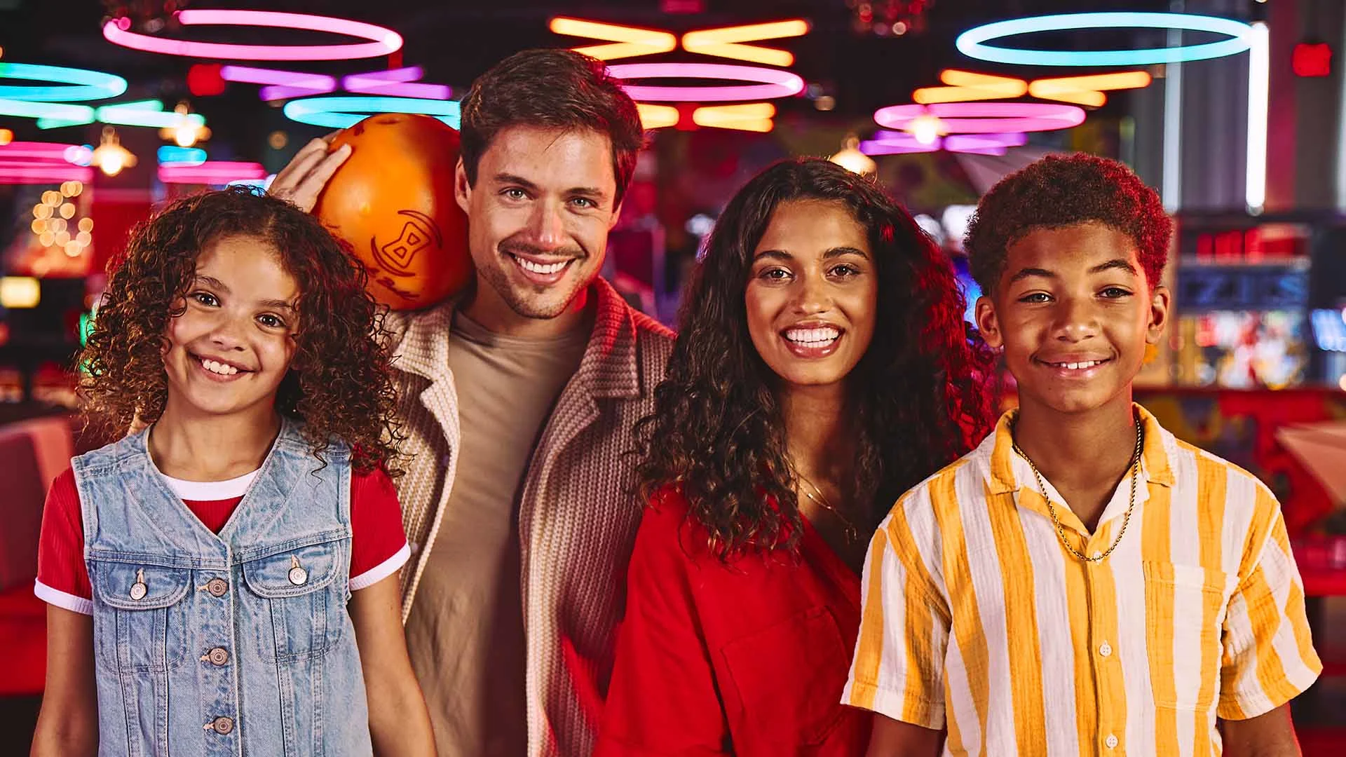 Family of four smiling with a bowling alley and neon lights in the background