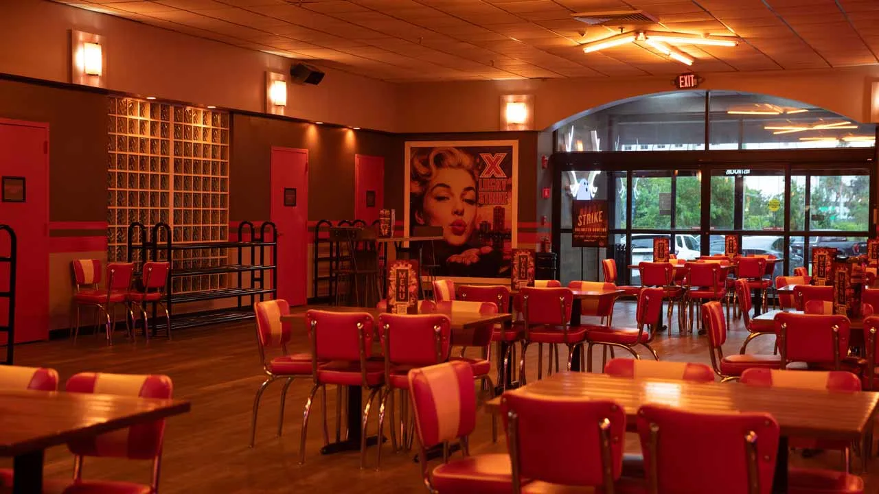 Retro-styled dining area at Lucky Strike Boca Raton with red vinyl chairs, wooden tables, and vintage-inspired wall art.