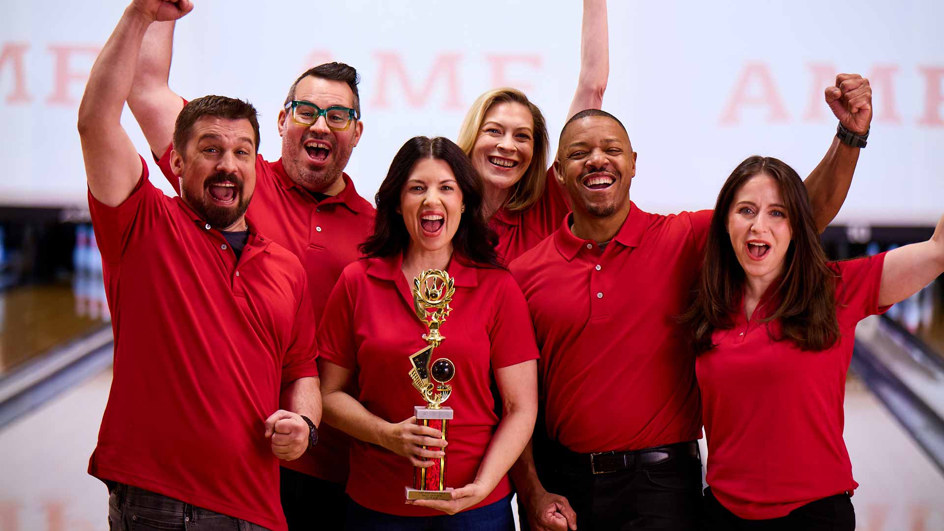 Group of bowlers celebrating a league win with a trophy inside a modern bowling alley