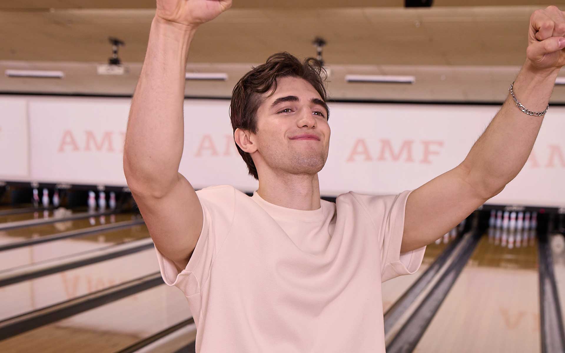 Young man celebrating a strike with arms raised at AMF bowling center.