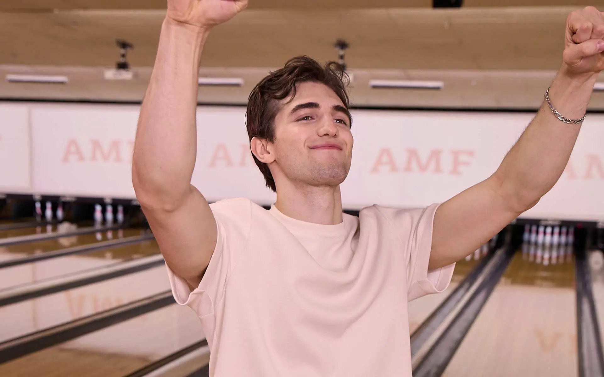Young man celebrating a strike with arms raised at AMF bowling center.
