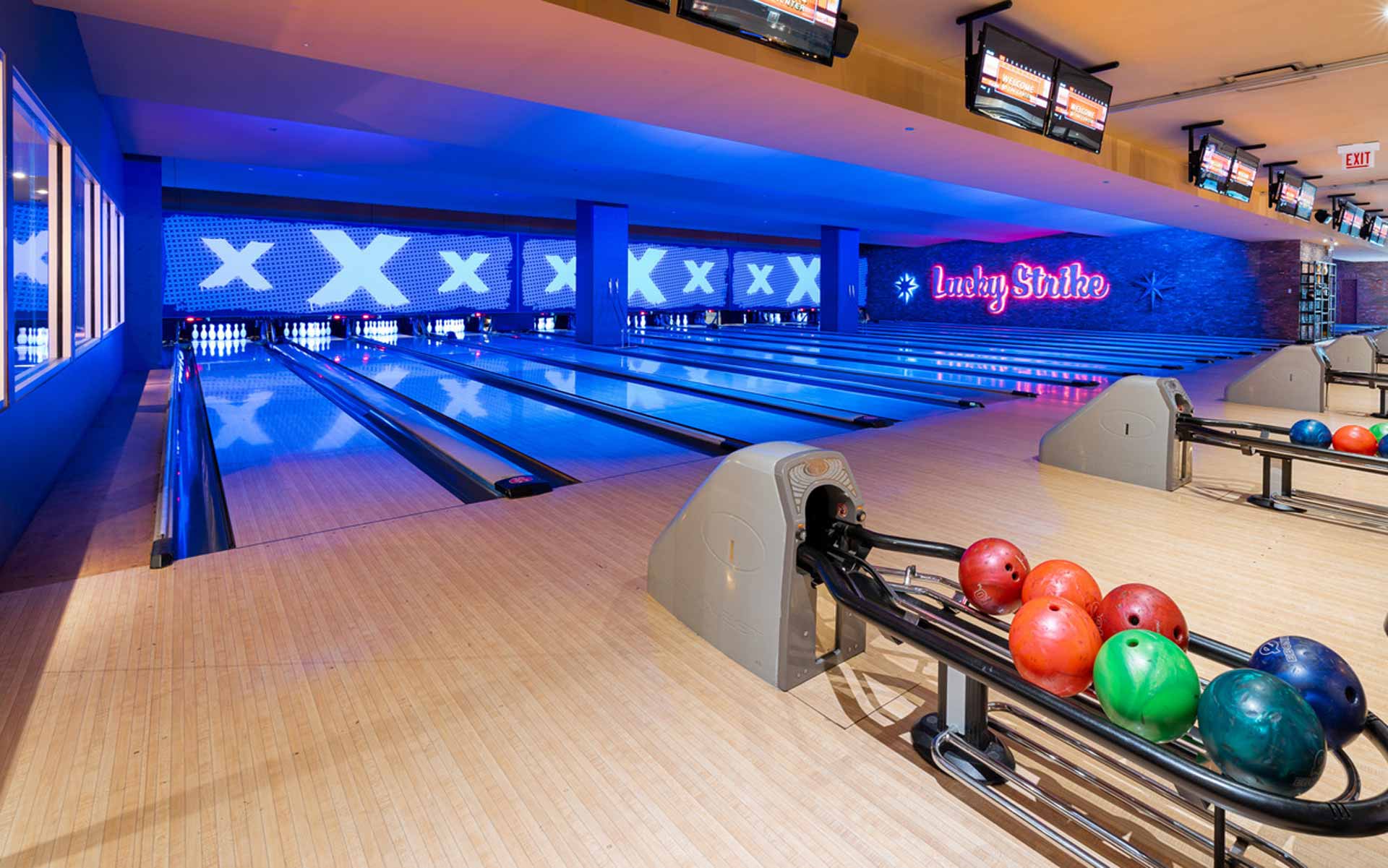 Wide view of sleek bowling lanes at Lucky Strike with blue neon lighting, scoring monitors, and polished wood lanes in a modern setting.