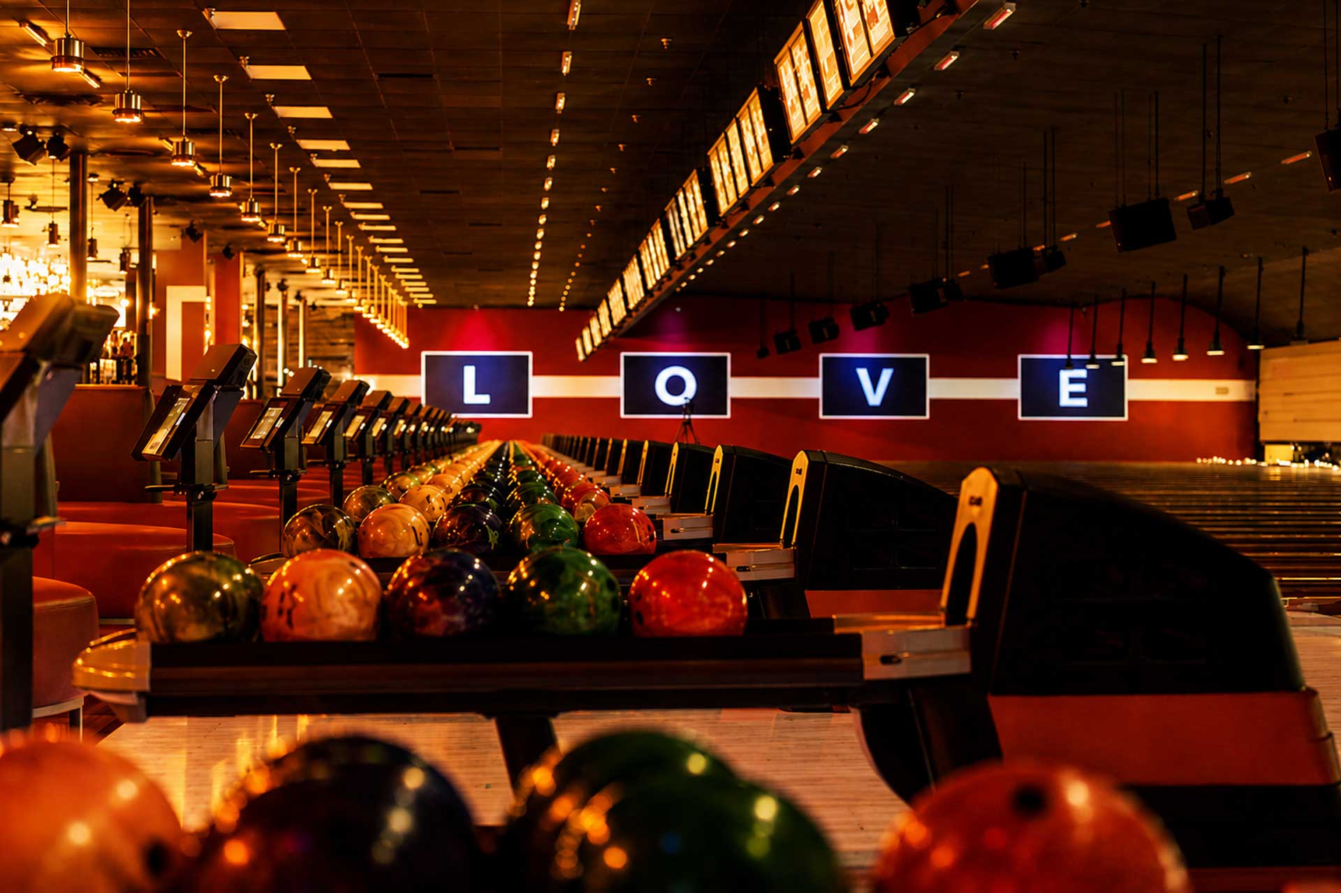 Colorful bowling balls lined up on return racks with a bowling center in the background.