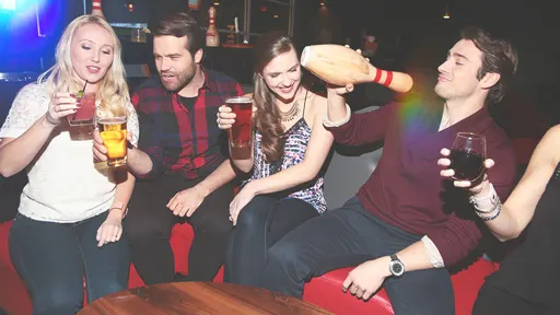 A group of adults drinking cocktails, beer and wine at a bowling alley.
