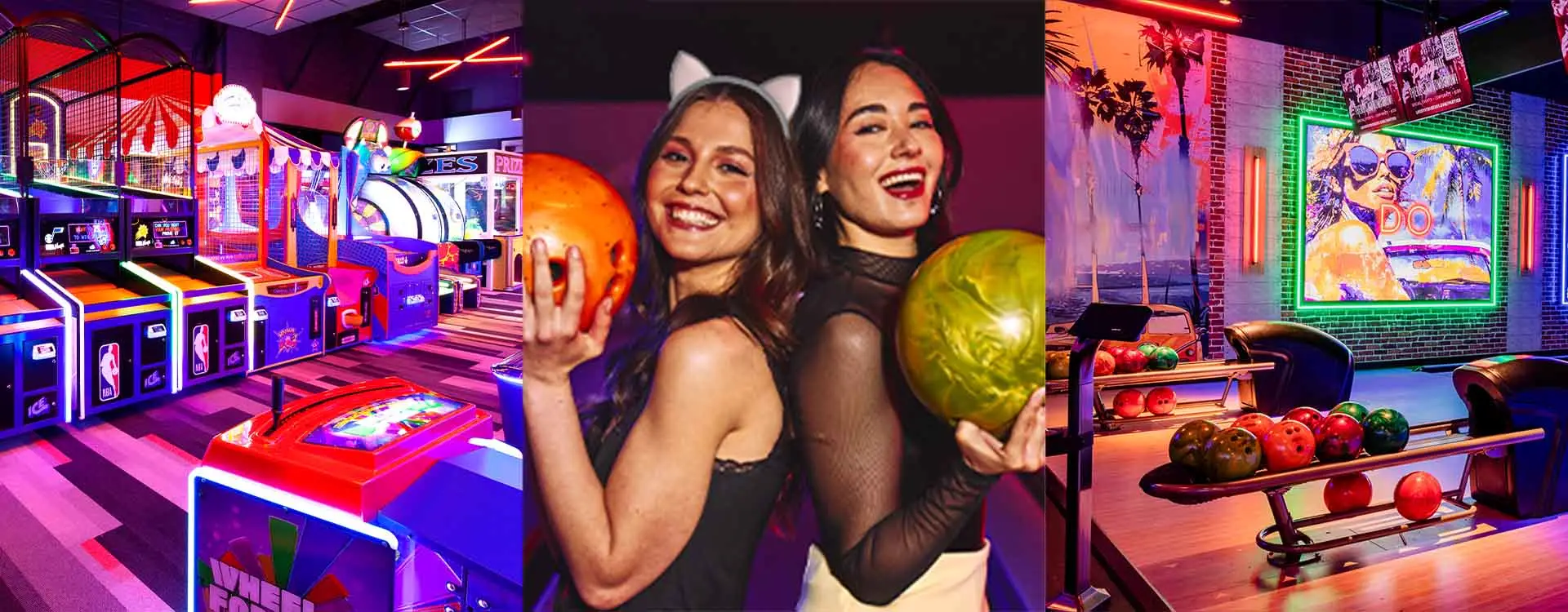 Two women in costume and holding bowling balls with an arcade an bowling lanes.