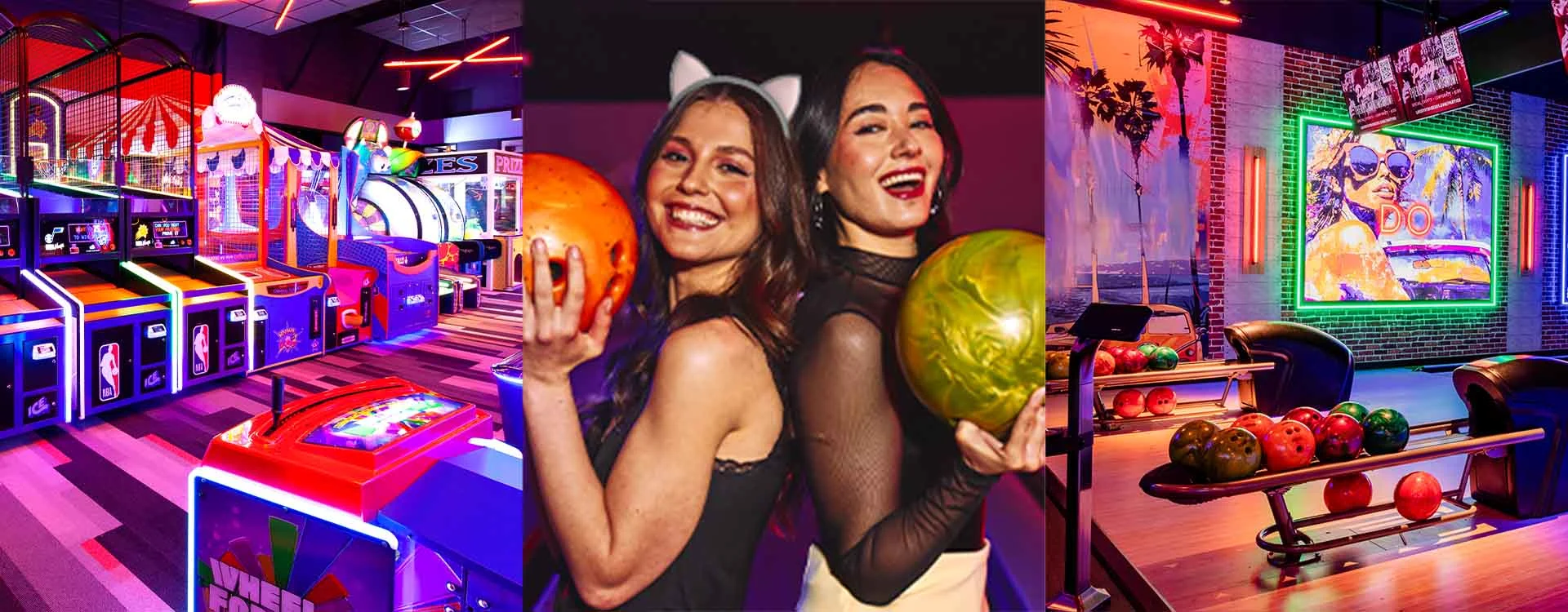 Two women in costume and holding bowling balls with an arcade an bowling lanes.