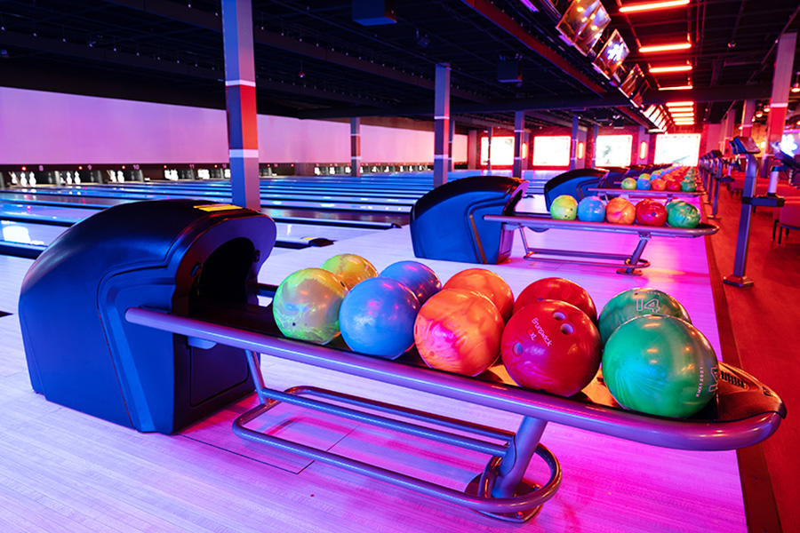 Colorful bowling balls on return rack with bowling center in the background.